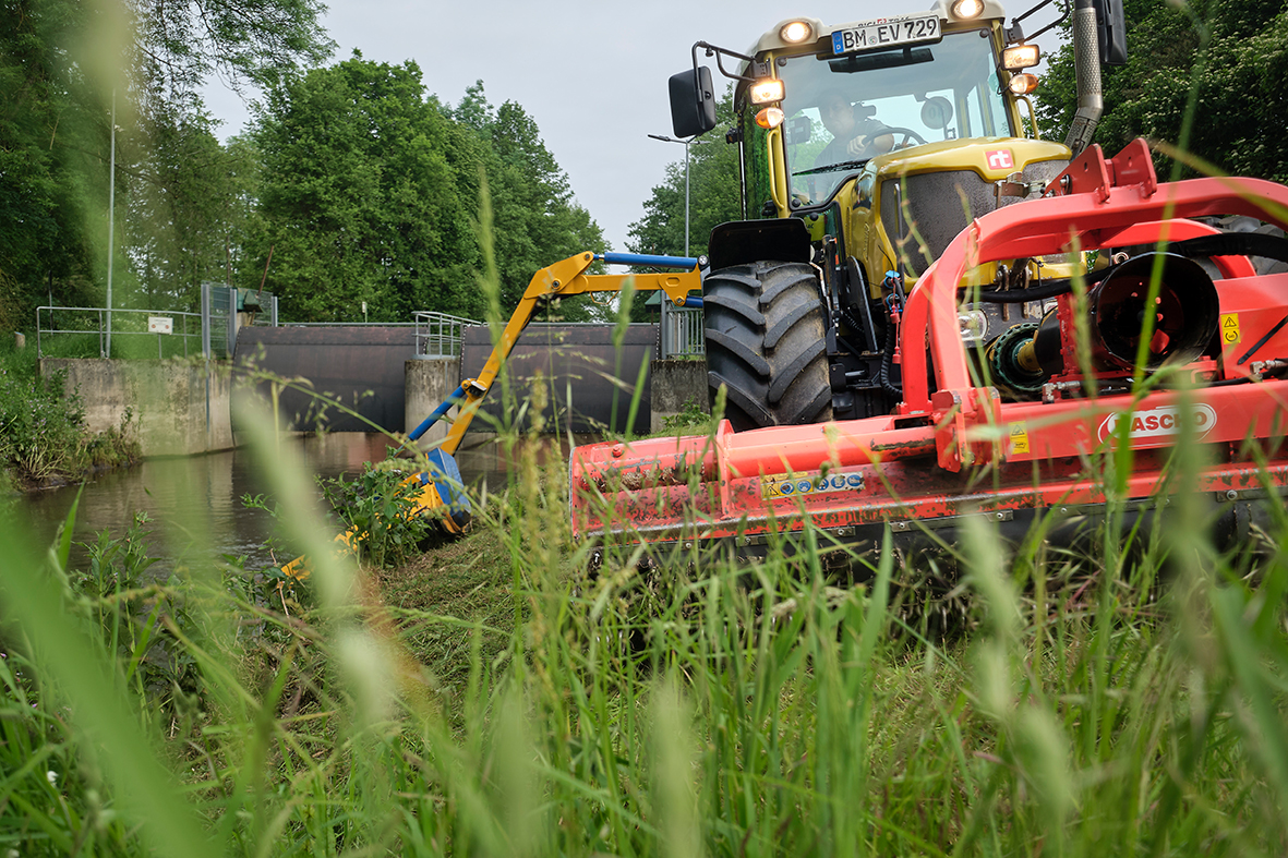 Trecker schneit Gras am Gewässer